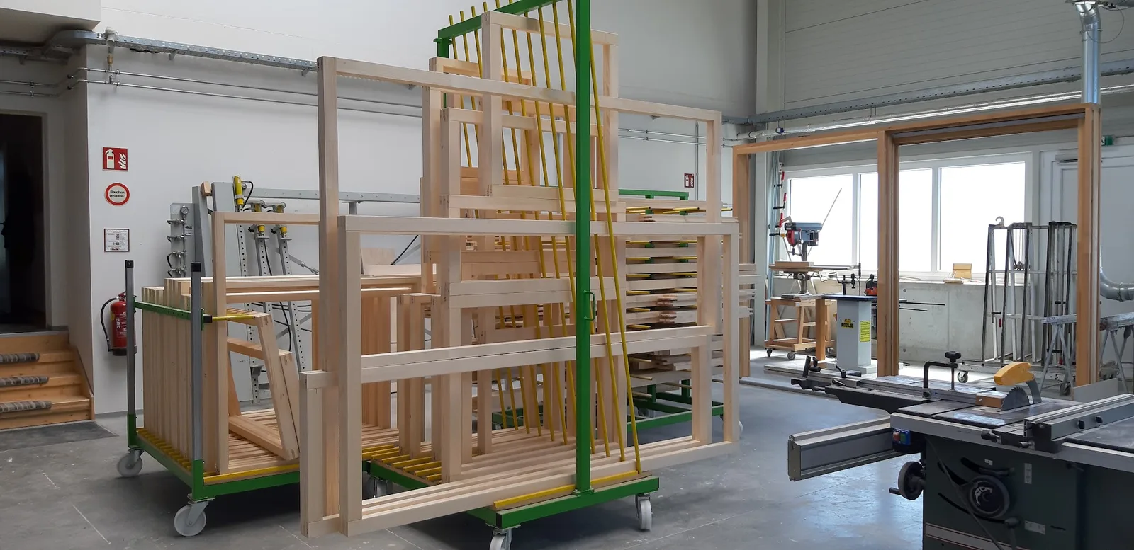 Werkstatt mit Fensterrahmen aus hellem Holz auf Transportwagen und Formatkreissäge