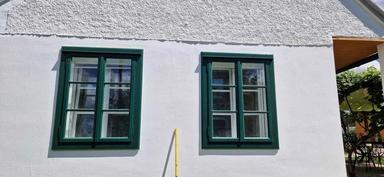 Zwei grüne Kastenfenster in weißer Fassade